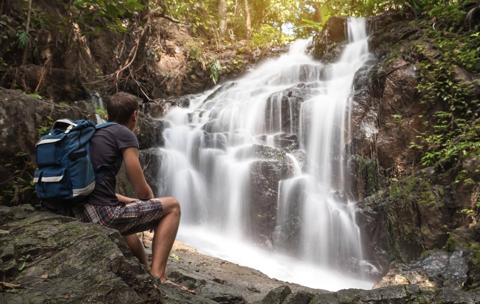 A man is sitting on the stone and looking on the Ton Sai waterfall in Phuket Thailand